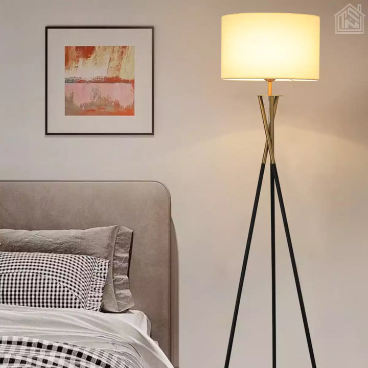 abajur de chão tripé preto com detalhe dourado ligado no quarto ao lado da cama