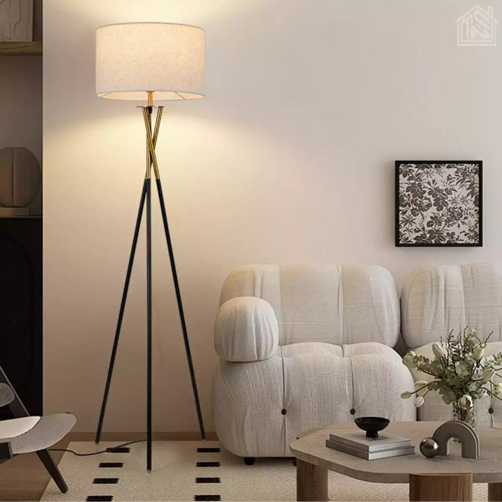 abajur de chão tripé preto com detalhe dourado em uma sala moderna ao lado de um sofá