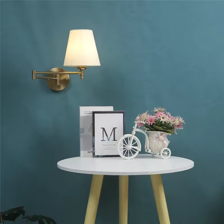 Arandela dourada em um ambiente sofisticado com mesa lateral branca e objetos de decoração