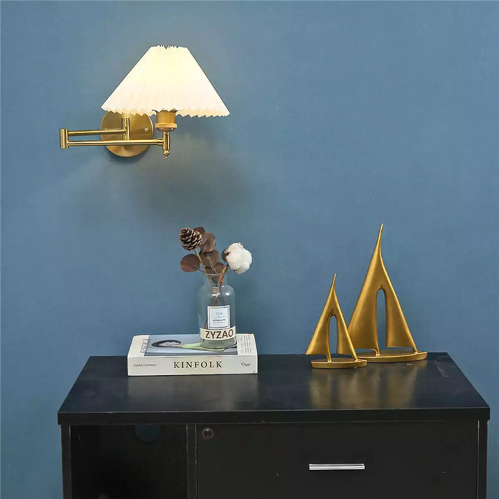 Arandela plissada dourada instalada em parede azul ao lado de um aparador com decoração