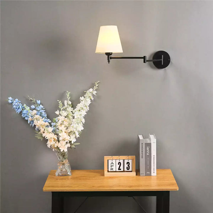 Luminária de parede articulada preta instalada em parede cinza com decoração ao lado